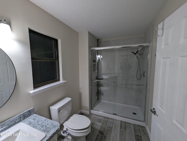 bathroom featuring a shower with door, vanity, a textured ceiling, and toilet