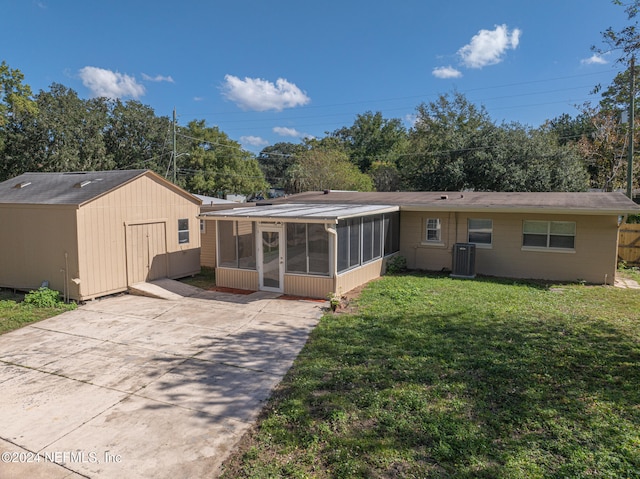 rear view of house with central AC unit, a sunroom, a yard, and a storage unit