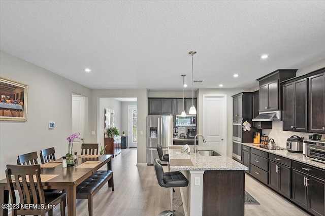 kitchen with light hardwood / wood-style floors, a center island with sink, a breakfast bar, appliances with stainless steel finishes, and decorative light fixtures