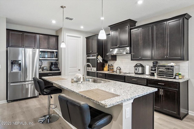 kitchen featuring stainless steel appliances, decorative light fixtures, an island with sink, a breakfast bar area, and light hardwood / wood-style flooring