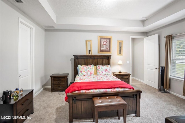 bedroom with a textured ceiling, light carpet, and a tray ceiling