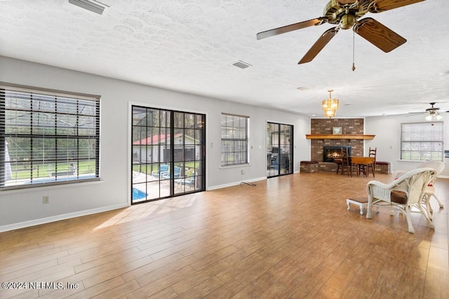 unfurnished living room featuring a fireplace, a textured ceiling, light hardwood / wood-style floors, and ceiling fan with notable chandelier