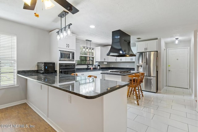 kitchen with pendant lighting, kitchen peninsula, appliances with stainless steel finishes, range hood, and white cabinetry