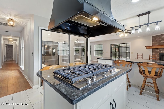 kitchen featuring island exhaust hood, light wood-type flooring, stainless steel gas cooktop, a fireplace, and white cabinetry