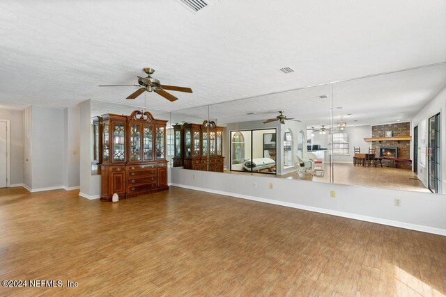 unfurnished living room featuring a fireplace, hardwood / wood-style floors, ceiling fan with notable chandelier, and a textured ceiling