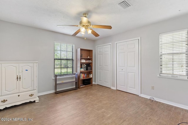 unfurnished bedroom with ceiling fan, hardwood / wood-style floors, and two closets