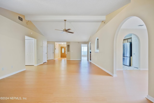 empty room featuring lofted ceiling with beams, ceiling fan, a textured ceiling, and light hardwood / wood-style flooring