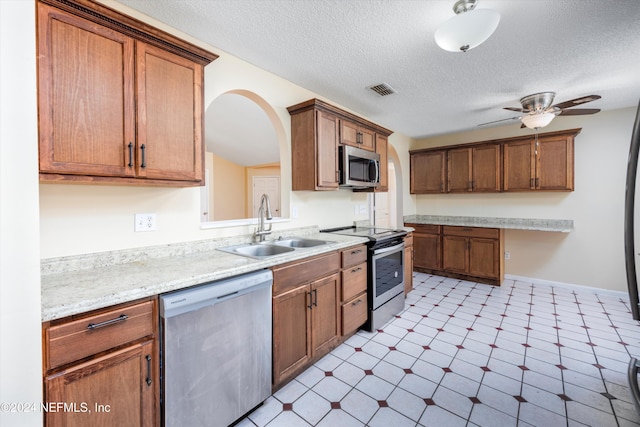 kitchen with light stone countertops, a textured ceiling, stainless steel appliances, ceiling fan, and sink