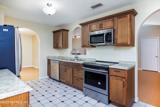 kitchen featuring a textured ceiling, stainless steel appliances, light hardwood / wood-style flooring, and sink