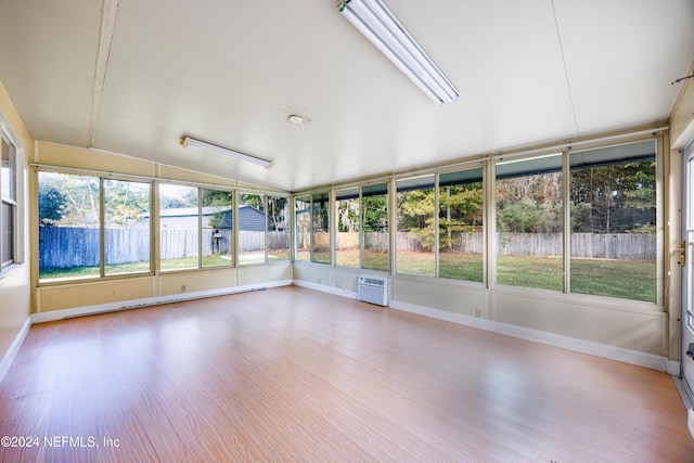 unfurnished sunroom featuring an AC wall unit, vaulted ceiling, and a healthy amount of sunlight