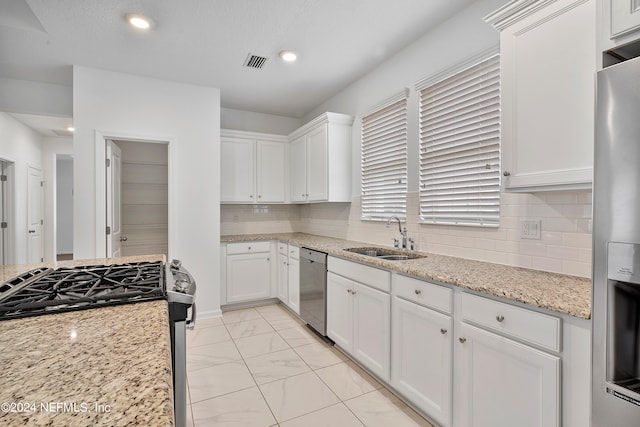 kitchen with sink, appliances with stainless steel finishes, tasteful backsplash, light stone counters, and white cabinetry