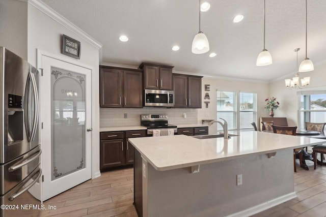 kitchen with dark brown cabinets, stainless steel appliances, a kitchen island with sink, sink, and decorative light fixtures