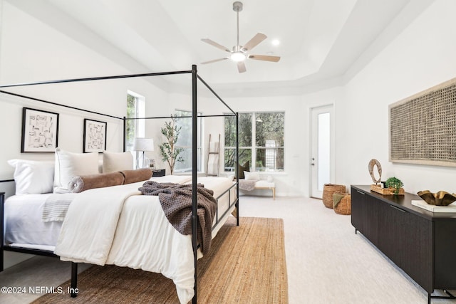 carpeted bedroom featuring a raised ceiling, multiple windows, and ceiling fan