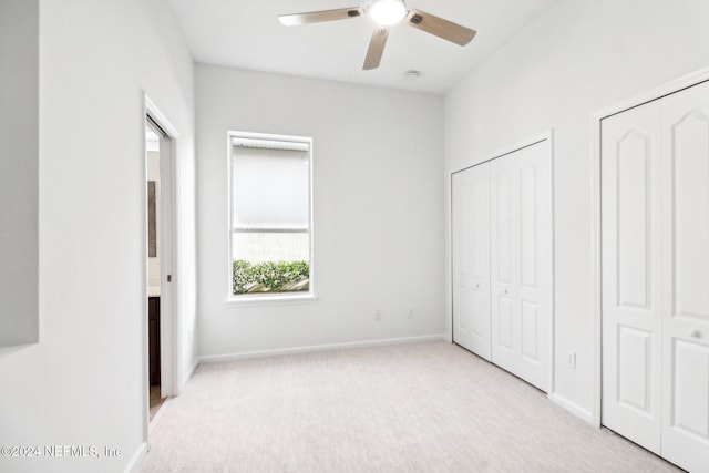 unfurnished bedroom featuring ceiling fan, light colored carpet, and multiple closets