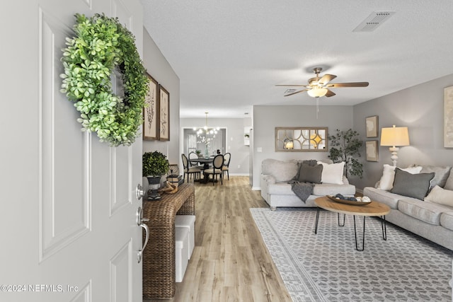 living room featuring a textured ceiling, ceiling fan with notable chandelier, light hardwood / wood-style flooring, and plenty of natural light