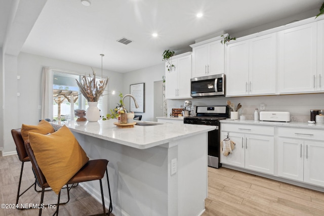 kitchen featuring white cabinets, light hardwood / wood-style flooring, an island with sink, appliances with stainless steel finishes, and decorative light fixtures