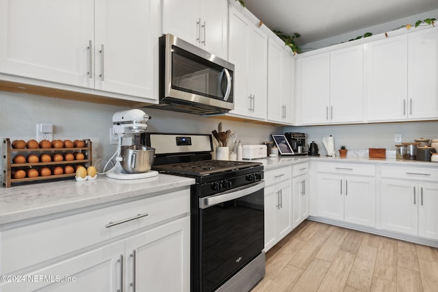 kitchen featuring light stone countertops, stainless steel appliances, white cabinetry, and light hardwood / wood-style floors