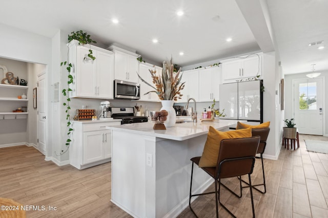 kitchen with white cabinetry, stove, an island with sink, a breakfast bar, and light wood-type flooring