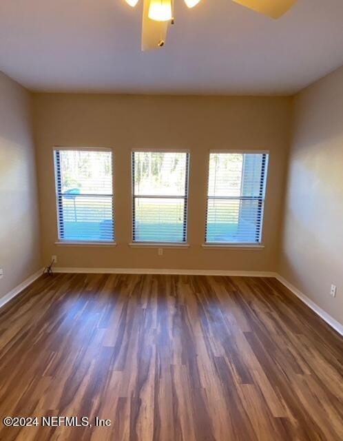 empty room featuring a wealth of natural light, ceiling fan, and dark wood-type flooring