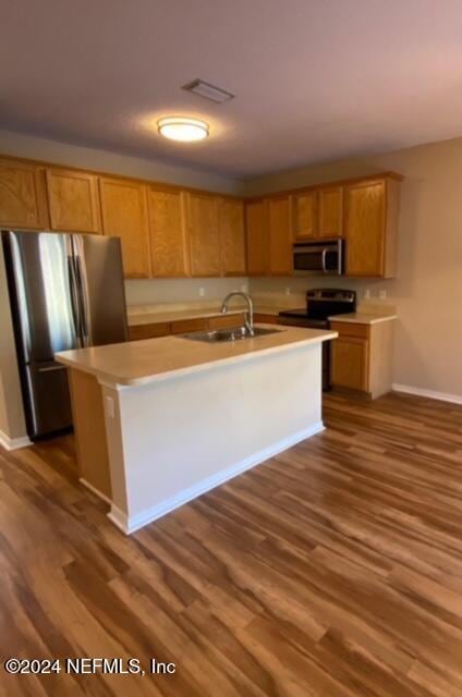 kitchen with a center island with sink, sink, appliances with stainless steel finishes, and dark wood-type flooring