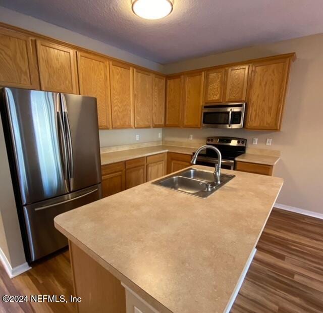 kitchen with appliances with stainless steel finishes, dark hardwood / wood-style flooring, a kitchen island with sink, and sink