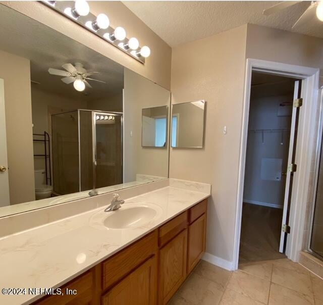 bathroom with tile patterned floors, an enclosed shower, a textured ceiling, toilet, and vanity