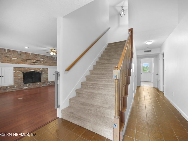 staircase featuring brick wall, wood-type flooring, ceiling fan, and a brick fireplace