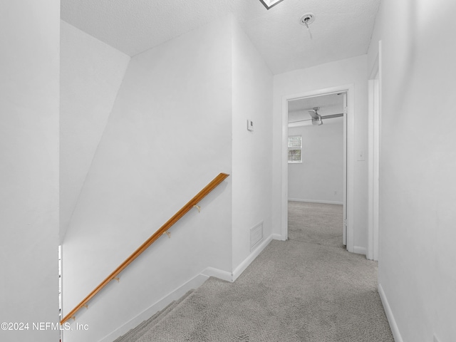 corridor featuring lofted ceiling, a textured ceiling, and light colored carpet