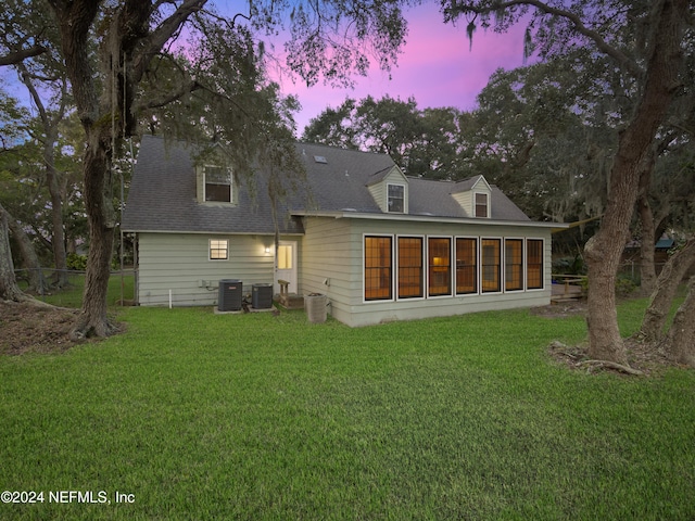 back house at dusk with a sunroom, cooling unit, and a lawn