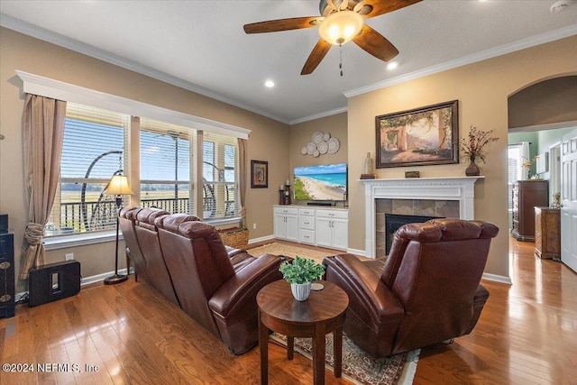 living room featuring a tiled fireplace, ceiling fan, light hardwood / wood-style floors, and ornamental molding