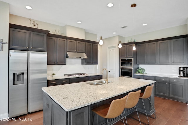 kitchen featuring light stone countertops, sink, stainless steel appliances, decorative light fixtures, and a center island with sink