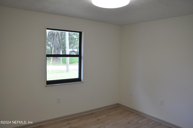 unfurnished room with light wood-type flooring and a textured ceiling