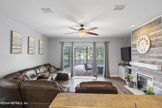 living room with a fireplace, ceiling fan, hardwood / wood-style floors, and a textured ceiling