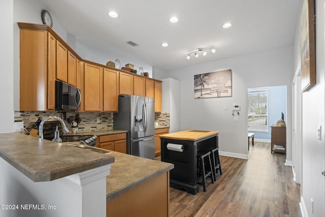 kitchen featuring dark hardwood / wood-style flooring, backsplash, stainless steel appliances, a center island, and a breakfast bar area