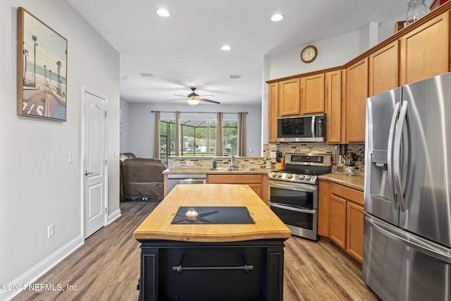 kitchen featuring appliances with stainless steel finishes, backsplash, ceiling fan, hardwood / wood-style flooring, and a kitchen island