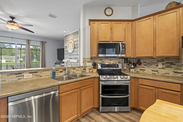 kitchen with backsplash, sink, light hardwood / wood-style flooring, and appliances with stainless steel finishes