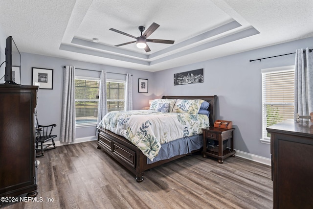 bedroom featuring a raised ceiling, ceiling fan, dark hardwood / wood-style flooring, and a textured ceiling