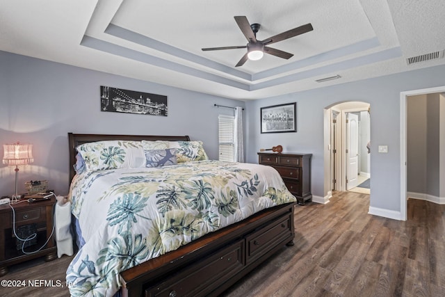 bedroom featuring a textured ceiling, a raised ceiling, ceiling fan, and dark wood-type flooring