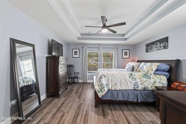 bedroom with a textured ceiling, ceiling fan, a tray ceiling, and dark hardwood / wood-style floors