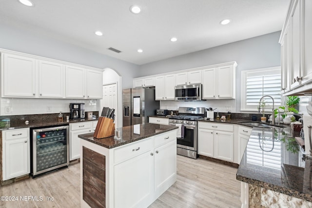 kitchen featuring dark stone counters, a kitchen island, white cabinetry, stainless steel appliances, and beverage cooler