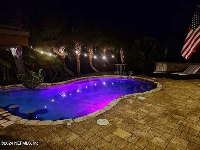 pool at night featuring a patio area