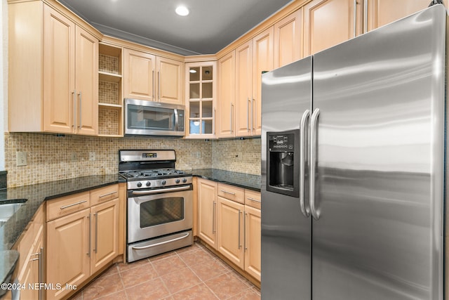 kitchen featuring light tile patterned flooring, appliances with stainless steel finishes, light brown cabinetry, and dark stone countertops