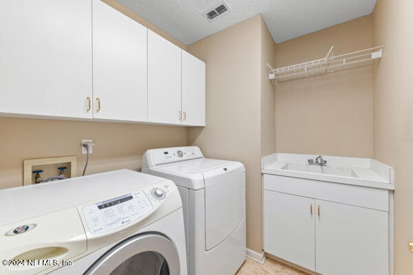 laundry room featuring washing machine and clothes dryer, sink, cabinets, and a textured ceiling