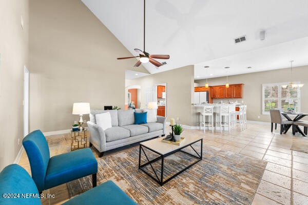 living room with light tile patterned floors, ceiling fan with notable chandelier, and high vaulted ceiling