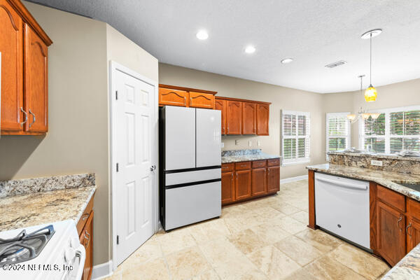 kitchen featuring pendant lighting, a notable chandelier, light stone countertops, and white appliances