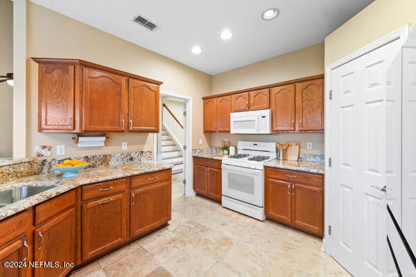 kitchen with light stone counters, sink, ceiling fan, and white appliances