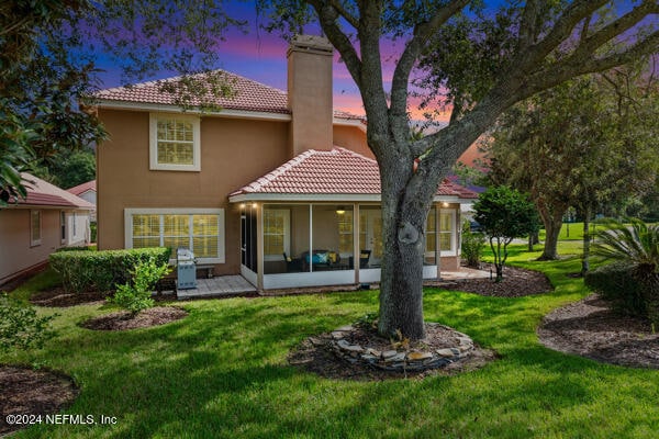 back house at dusk with a lawn and a sunroom