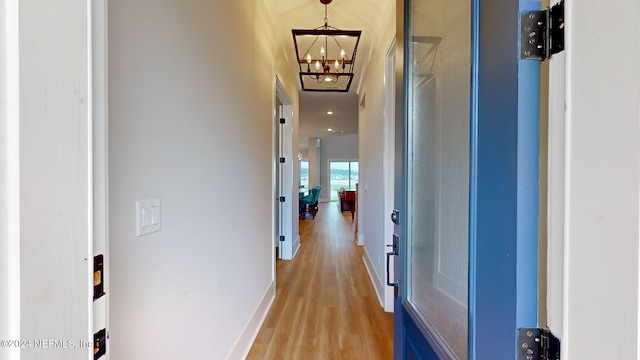 hall with a notable chandelier, baseboards, and light wood-style floors