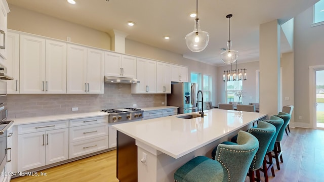 kitchen featuring under cabinet range hood, stainless steel appliances, white cabinets, tasteful backsplash, and an island with sink