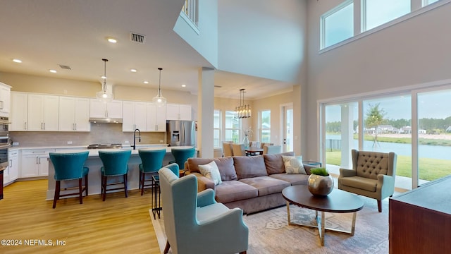 living room featuring a notable chandelier, recessed lighting, visible vents, a towering ceiling, and light wood-type flooring